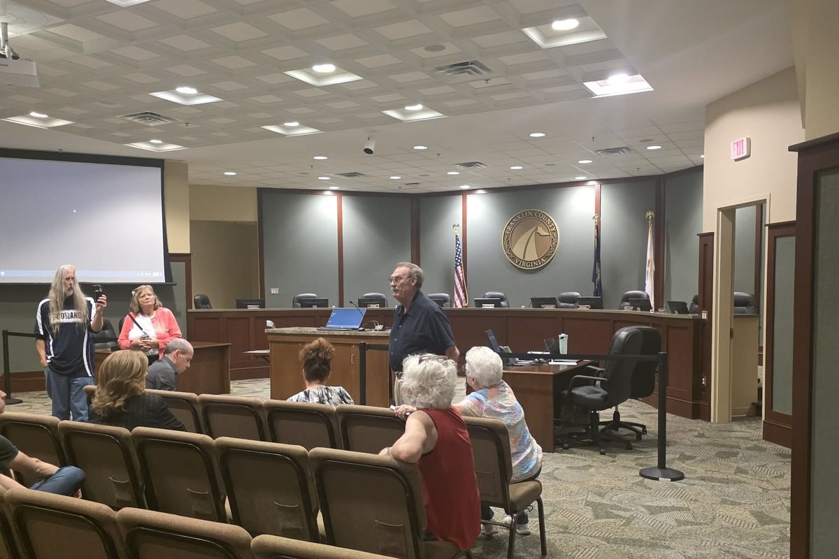 An empty Franklin County Board of Supervisors dais while residents stand and talk among themselves in the meeting room.
